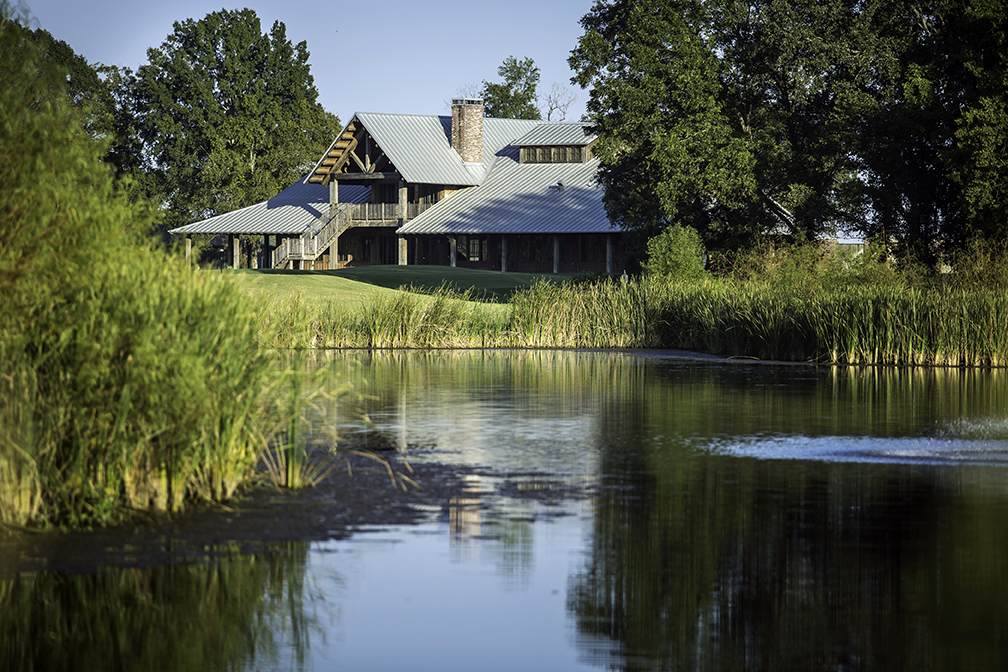 Black Bear Golf Club Lodge surrounded by large trees, on the shores of a calm lake.