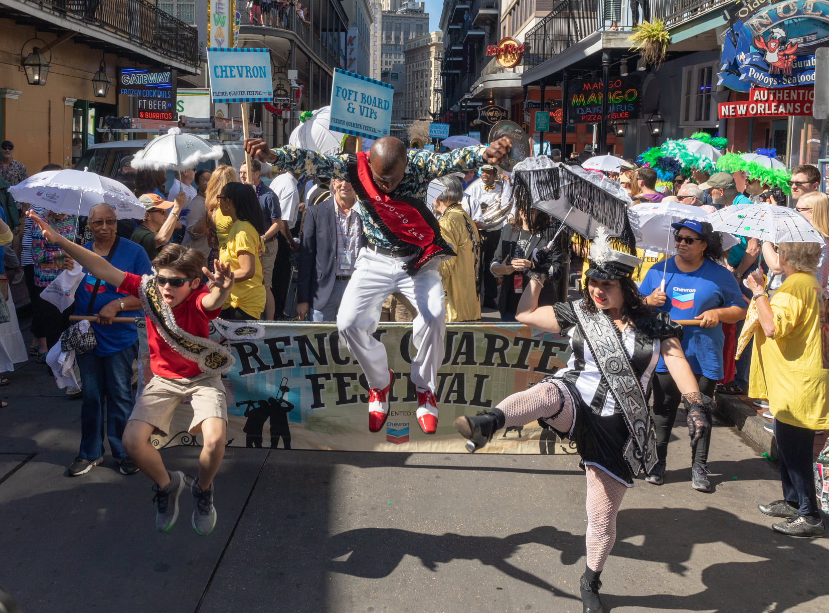 Participants in the French Quarter Festival parade hold signs and dance in the street.