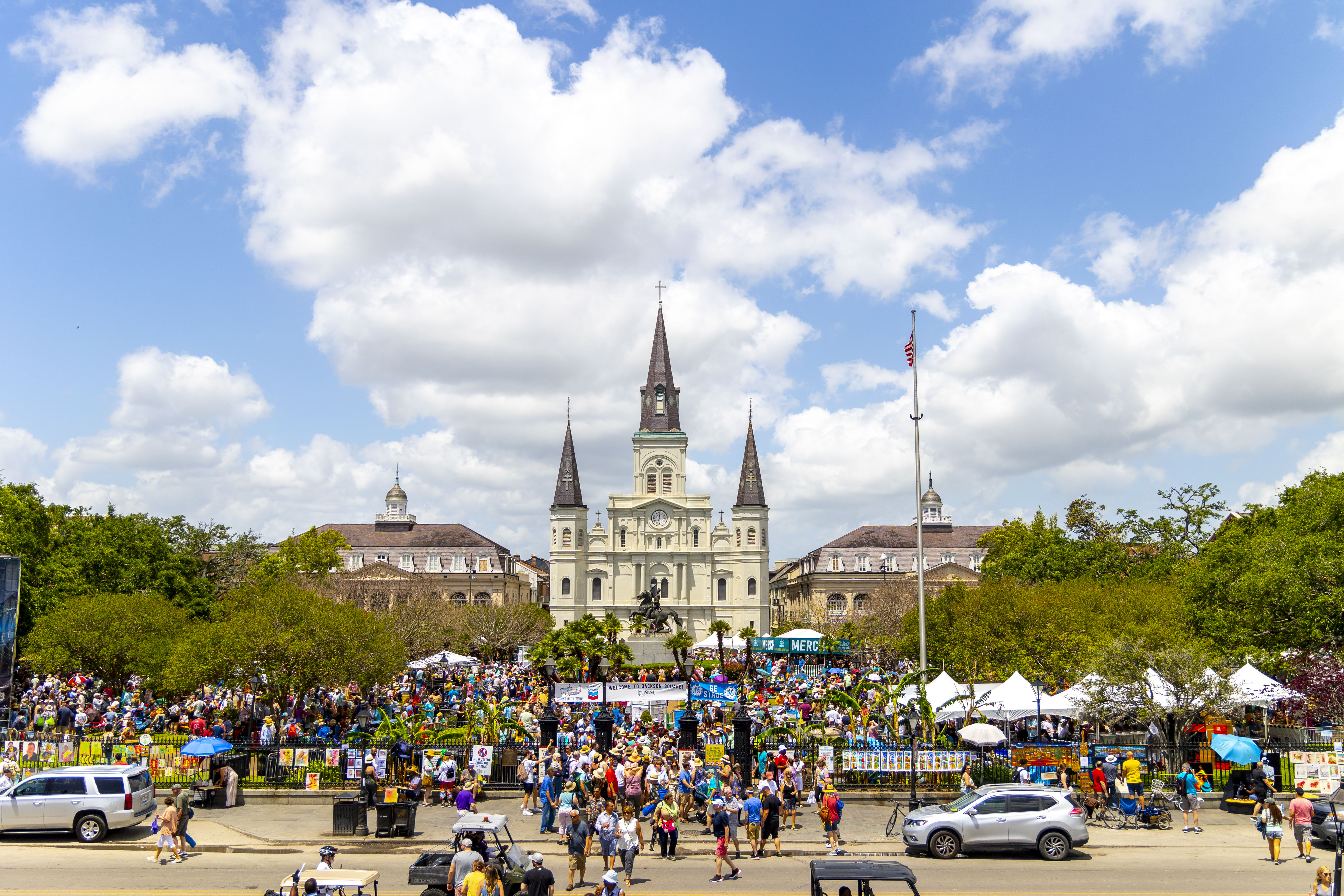 Crowds of people line the streets for the French Quarter Festival in New Orleans, with St. Louis Cathedral in the background.