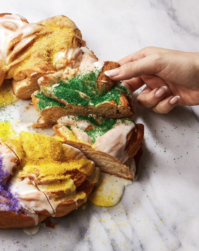 Someone grabs a slice of green-sprinkled king cake.