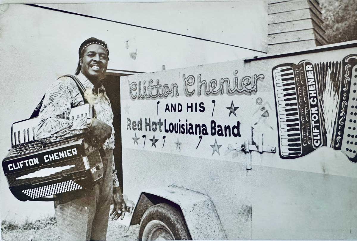 Clifton Chenier poses with an accordion in front of a vehicle with Clifton Chenier and his red hot Louisiana Band on it