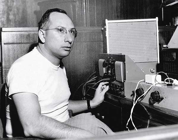 Cosimo, in a white T shirt and tweed pants, sits in front of recording equipment