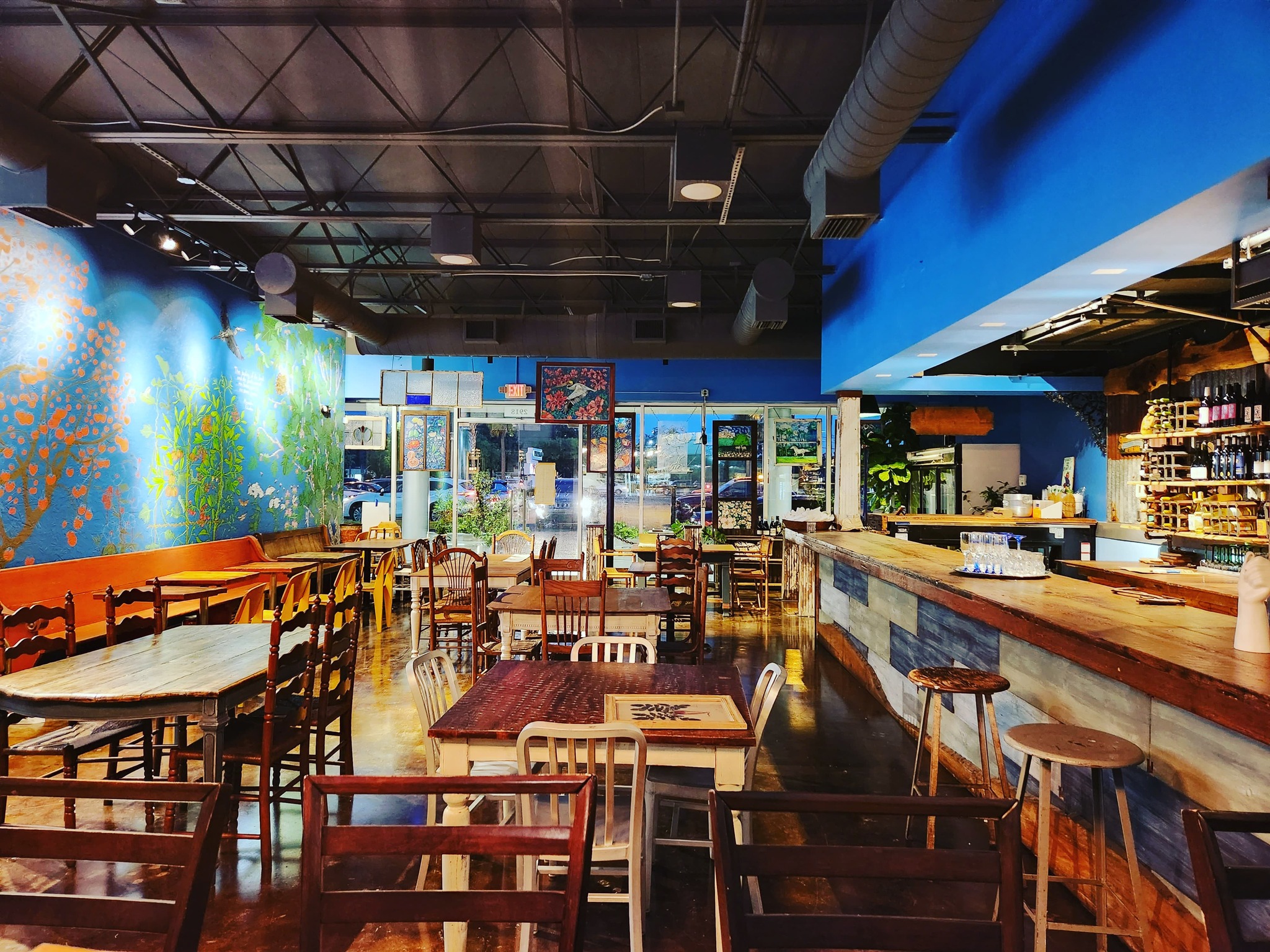 A clean bar and wooden tables and chairs surrounded by blue walls with murals at Scratch Farm Kitchen