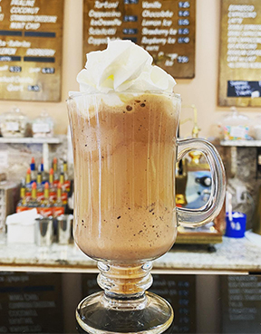 A coffee drink topped with a pile of whipped cream sits in a decorative glass on the counter of Angelo Brocato in New Orleans.