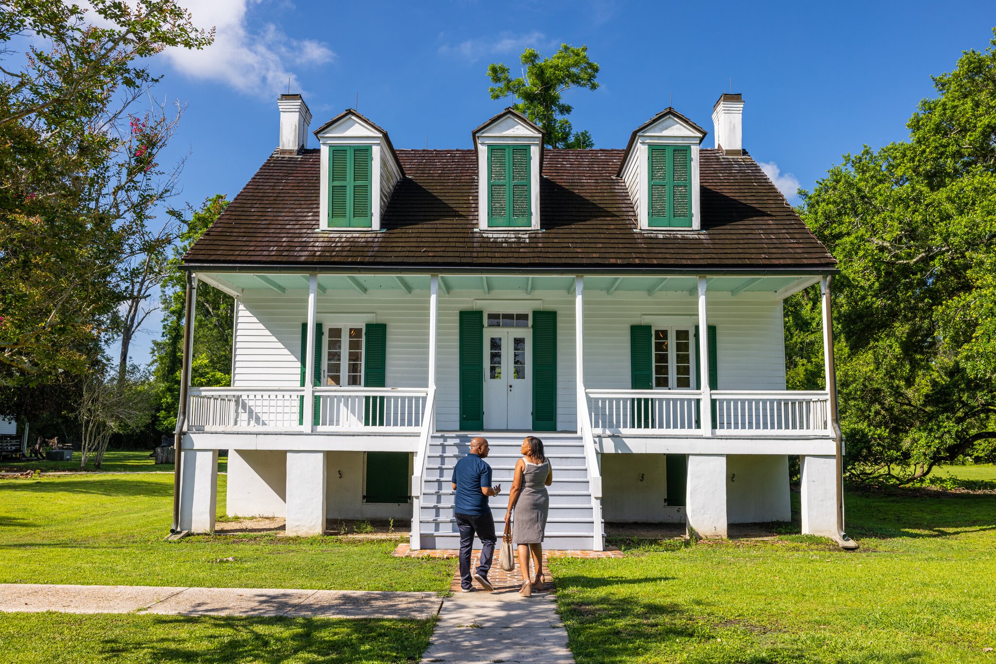 A couple stands in front of the home at E.D. White Historic Site, a white building with green shutters.