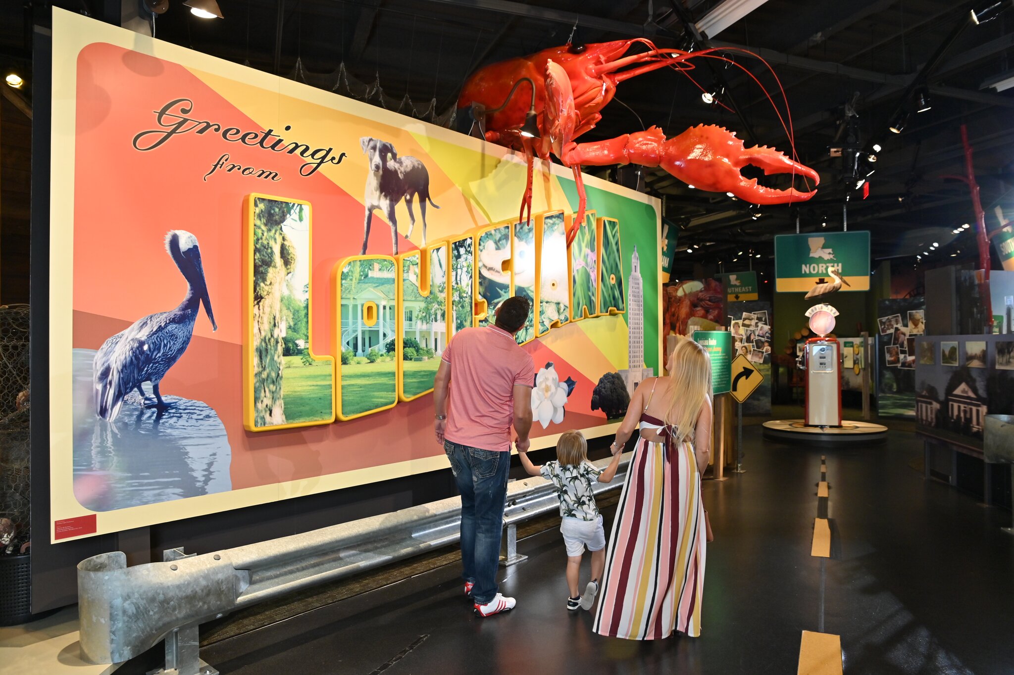 Madame John's Legacy in the French Quarter A woman looking at a large museum exhibit shaped like a postcard, with text that reads “Greetings from Louisiana” and has a red crawfish on top