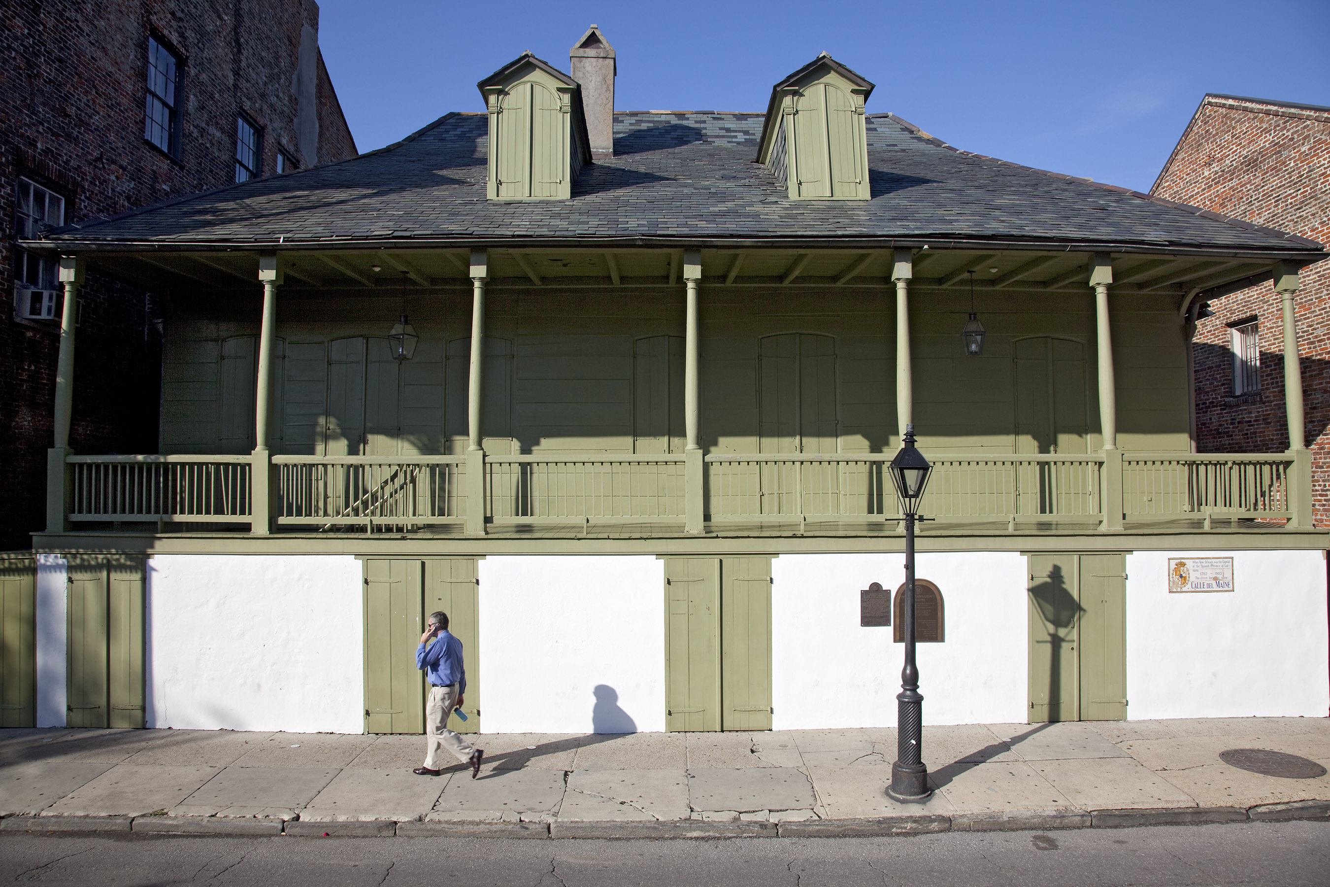 Man walking past a sage-green building with a large porch