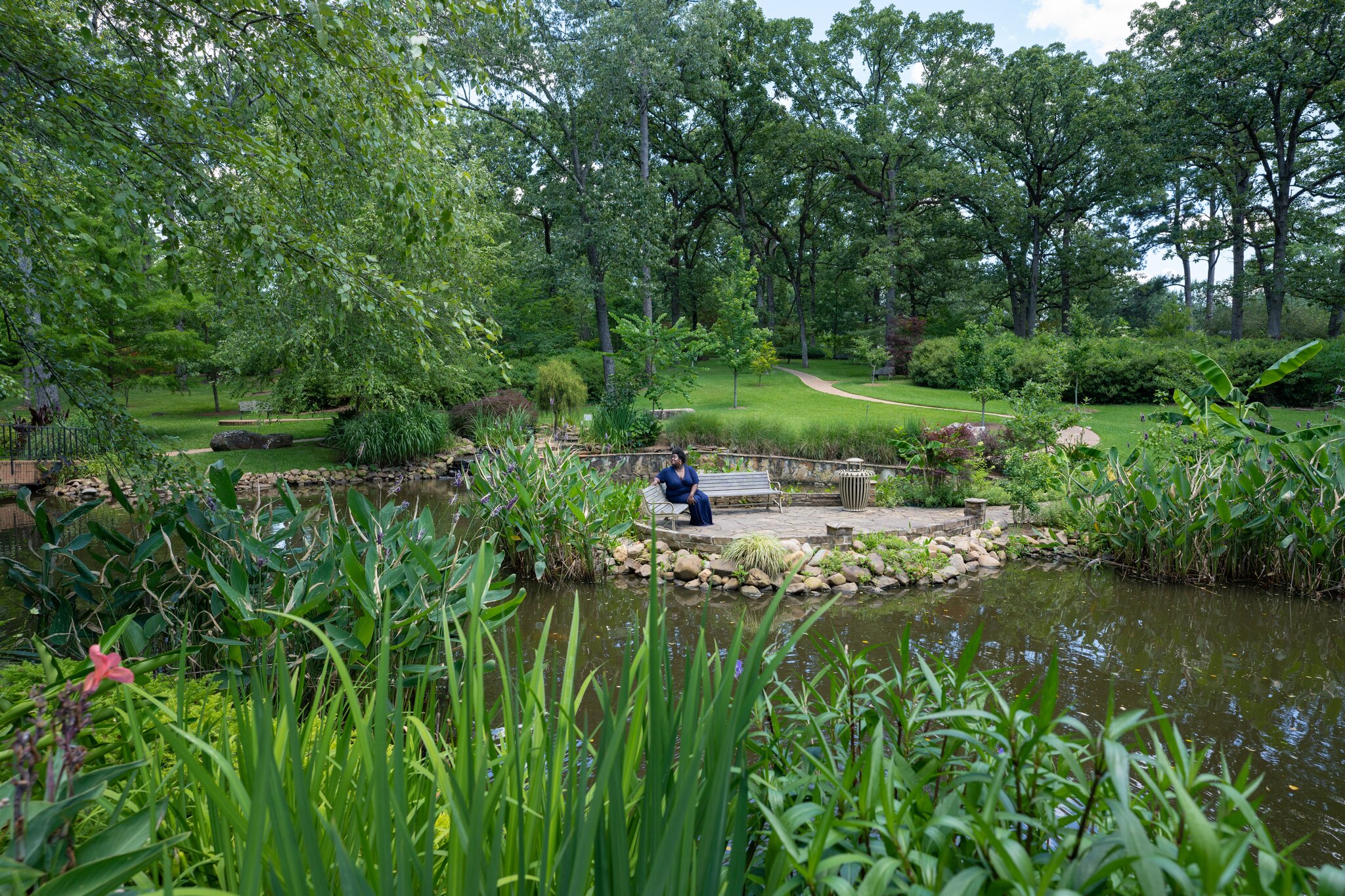 A woman in a blue dress relaxes on a bench by the pond at the R.W. Norton Art Gallery and Botanic Gardens in Shreveport.