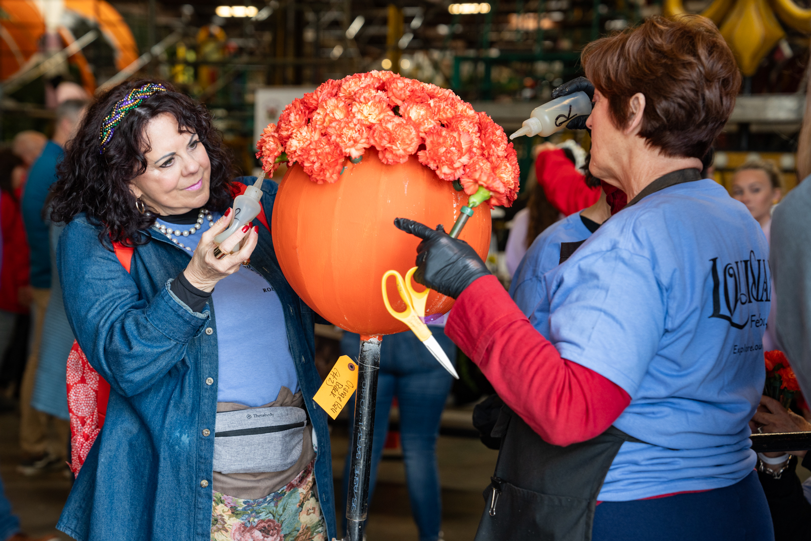 Two volunteers add orange and white flowers to a component of the 2024 Explore Louisiana Rose Parade float.