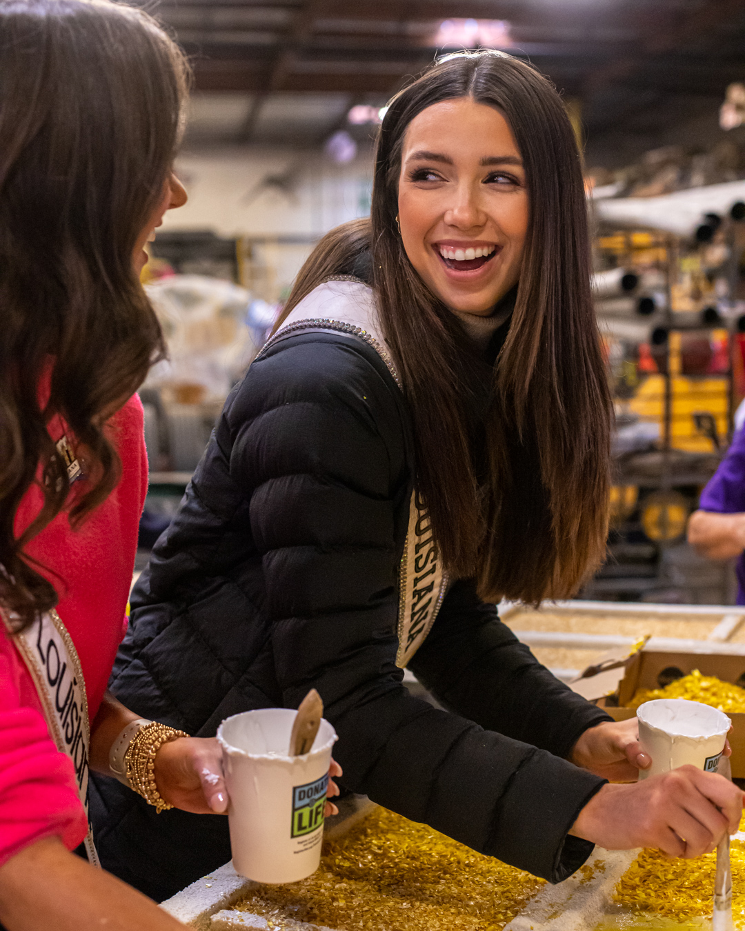 Two volunteers laugh while adding gold glitter to a component of the 2023 Explore Louisiana Rose Parade float.