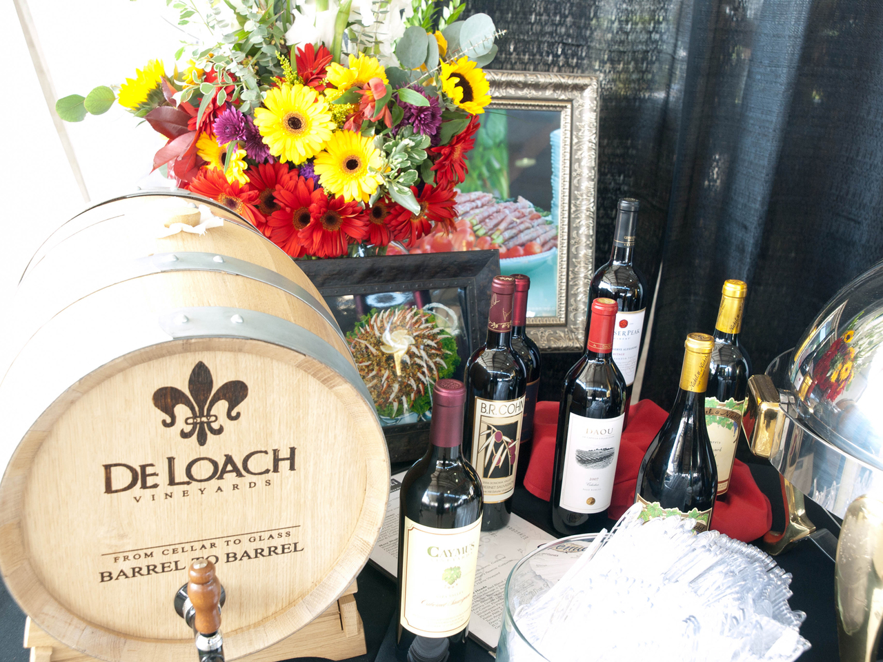 A wine display at CORK Wine Festival, featuring several bottles of red and white wine and a barrel advertising De Loach Vineyards.