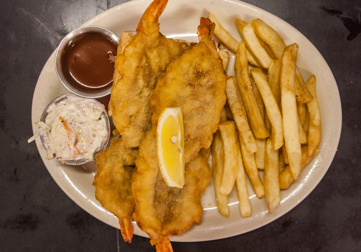 A Shrimp Buster sandwich with fries, coleslaw and dipping sauce, garnished with a lemon.