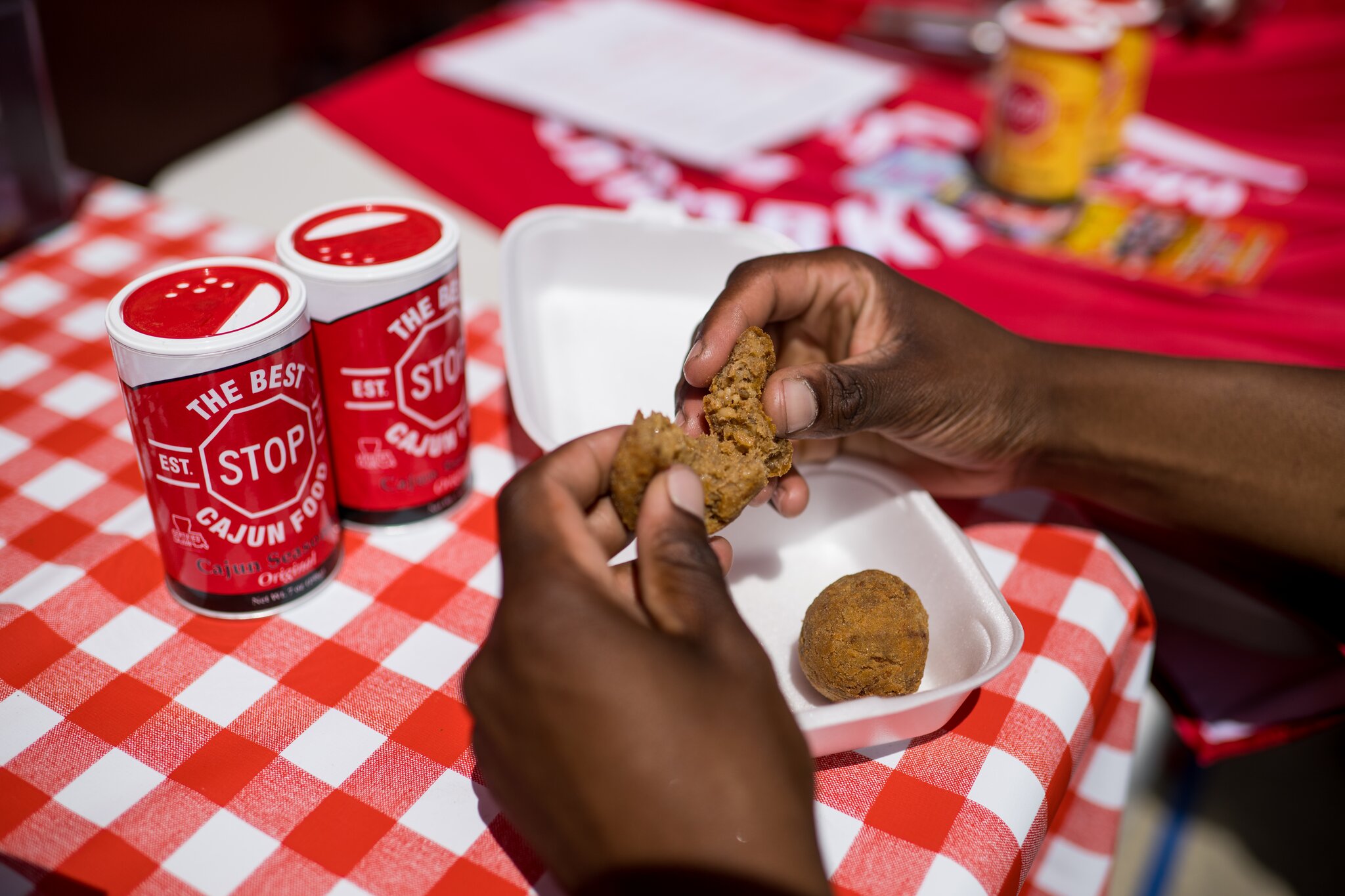 Hands break a boudin ball apart against a white- and red-checkered tablecloth.