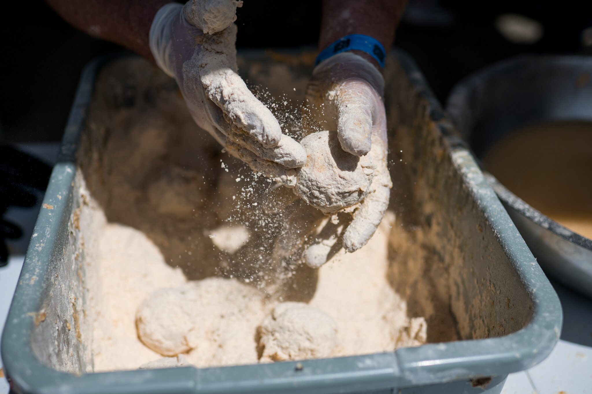 Gloved hands toss a boudin ball in seasoned flour.