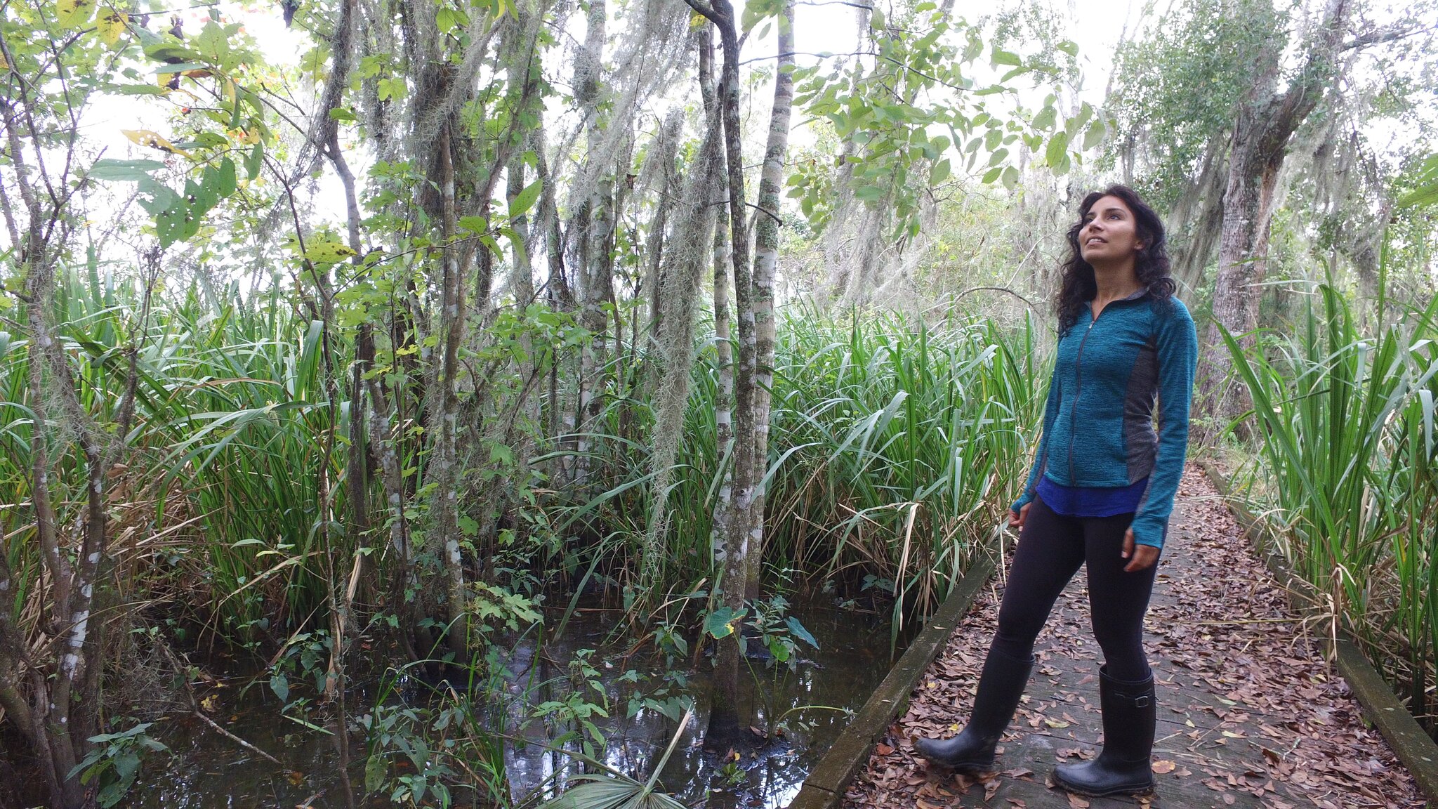 A woman in a blue jacket and black rainboots gazes at the surrounding nature in Mandalay National Wildlife Refuge.