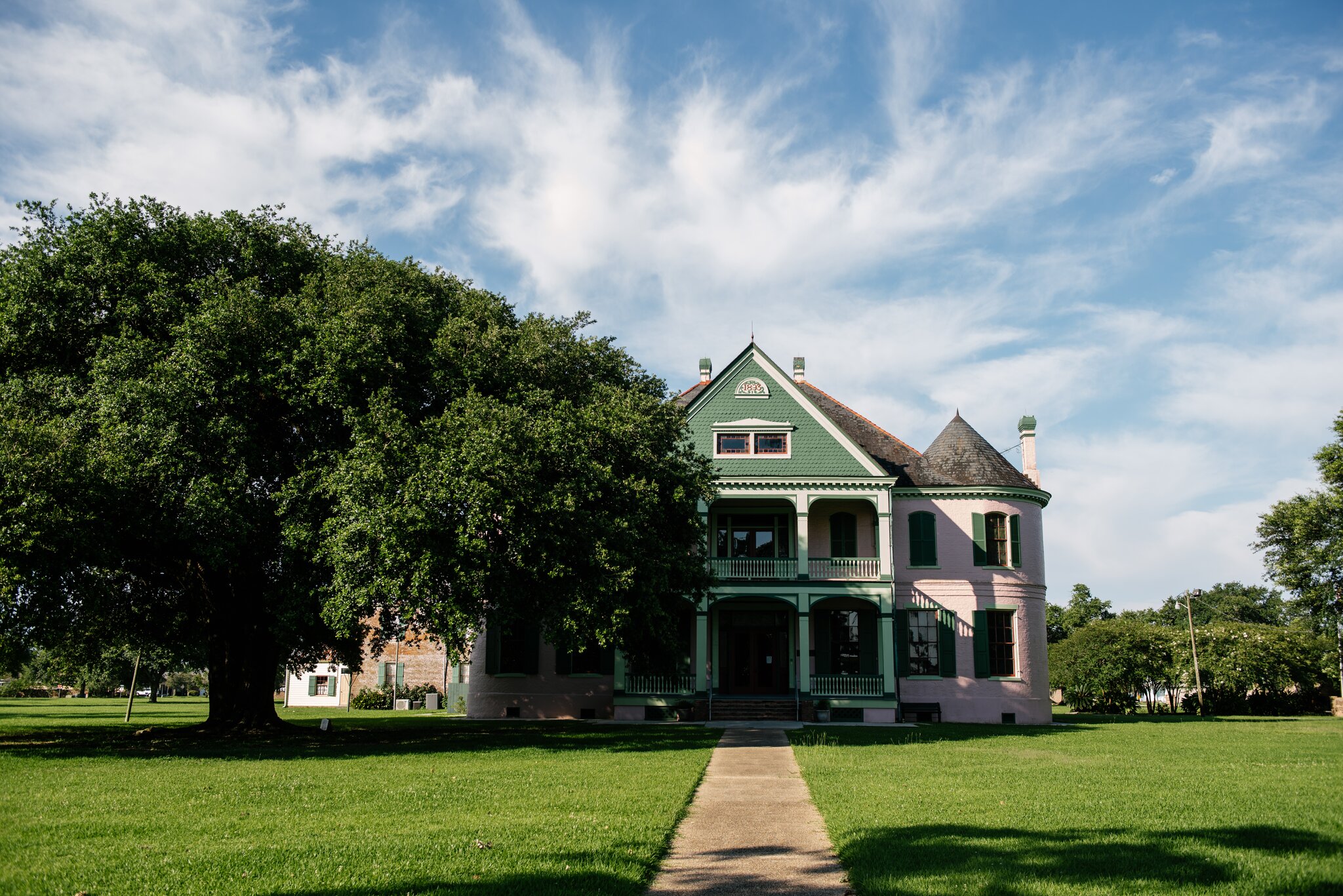Southdown Plantation, a green and pink building, is partially shaded by a large green tree.
