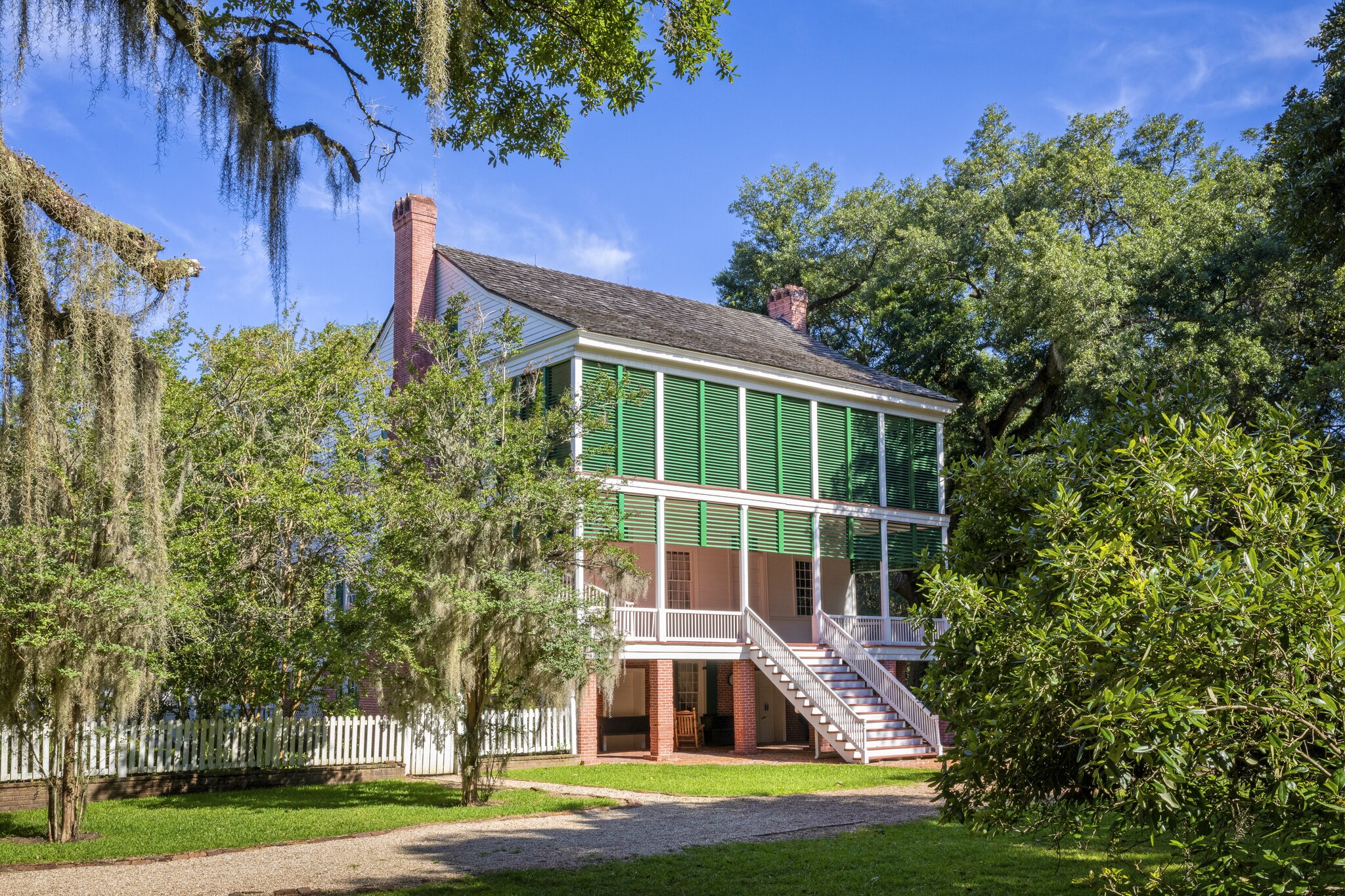 The Oakley House at the Audubon Historic Site, with bright green window panes, surrounded by lush green trees and shrubs.