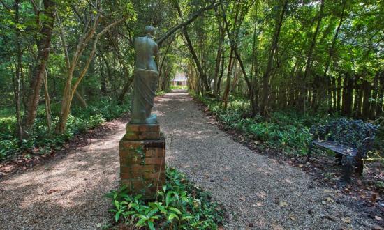 A grayish green statue stands at the entrance to a trail at the Audubon Historic Site.