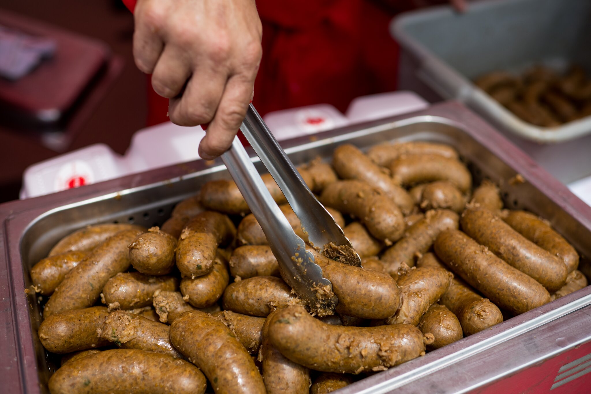 A hand uses tongs to serve links of boudin sausage from a steaming tray.