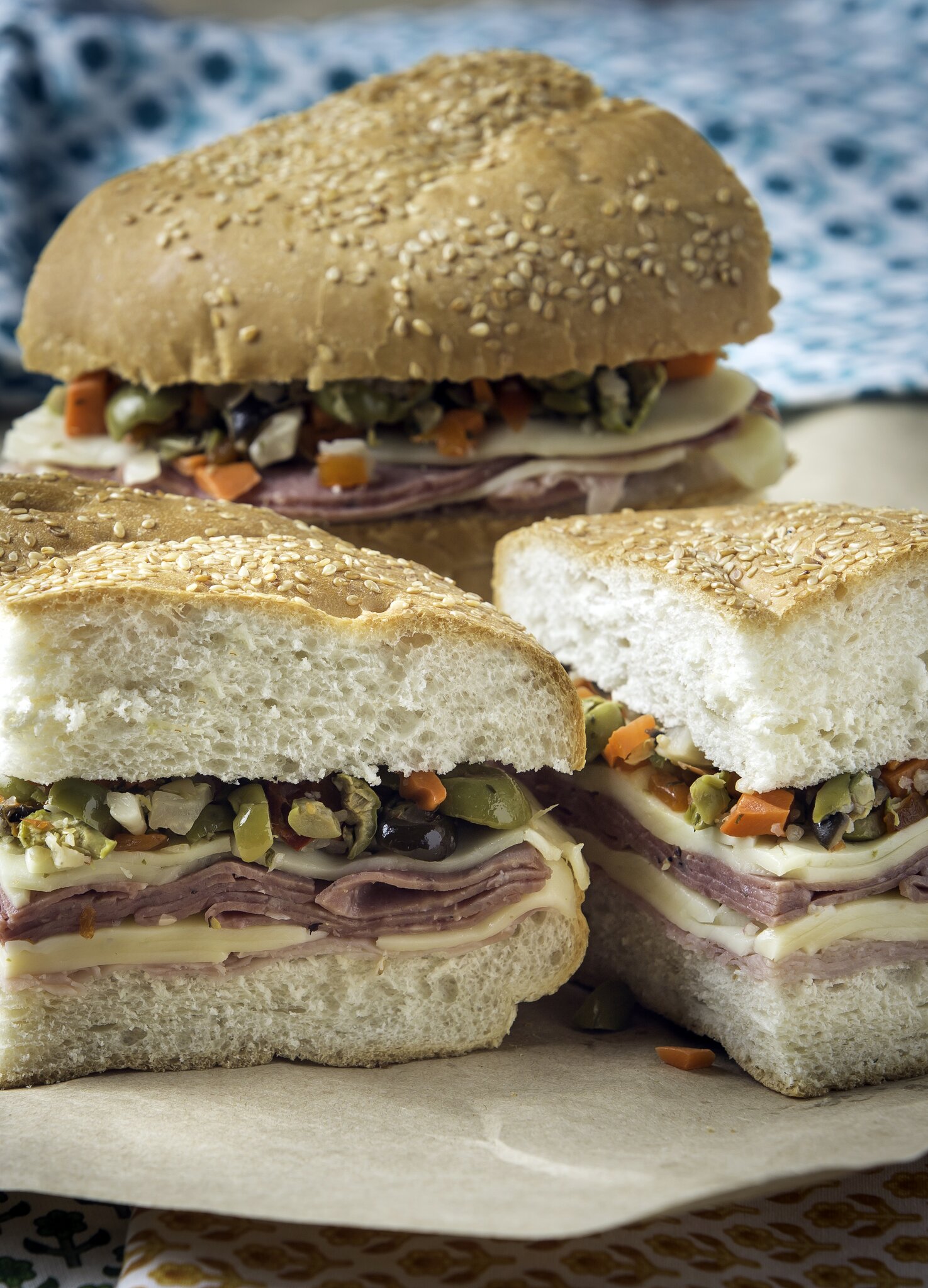Sliced muffuletta sandwiches stacked with layers of meat, cheese and olive tapenade on sesame bread.