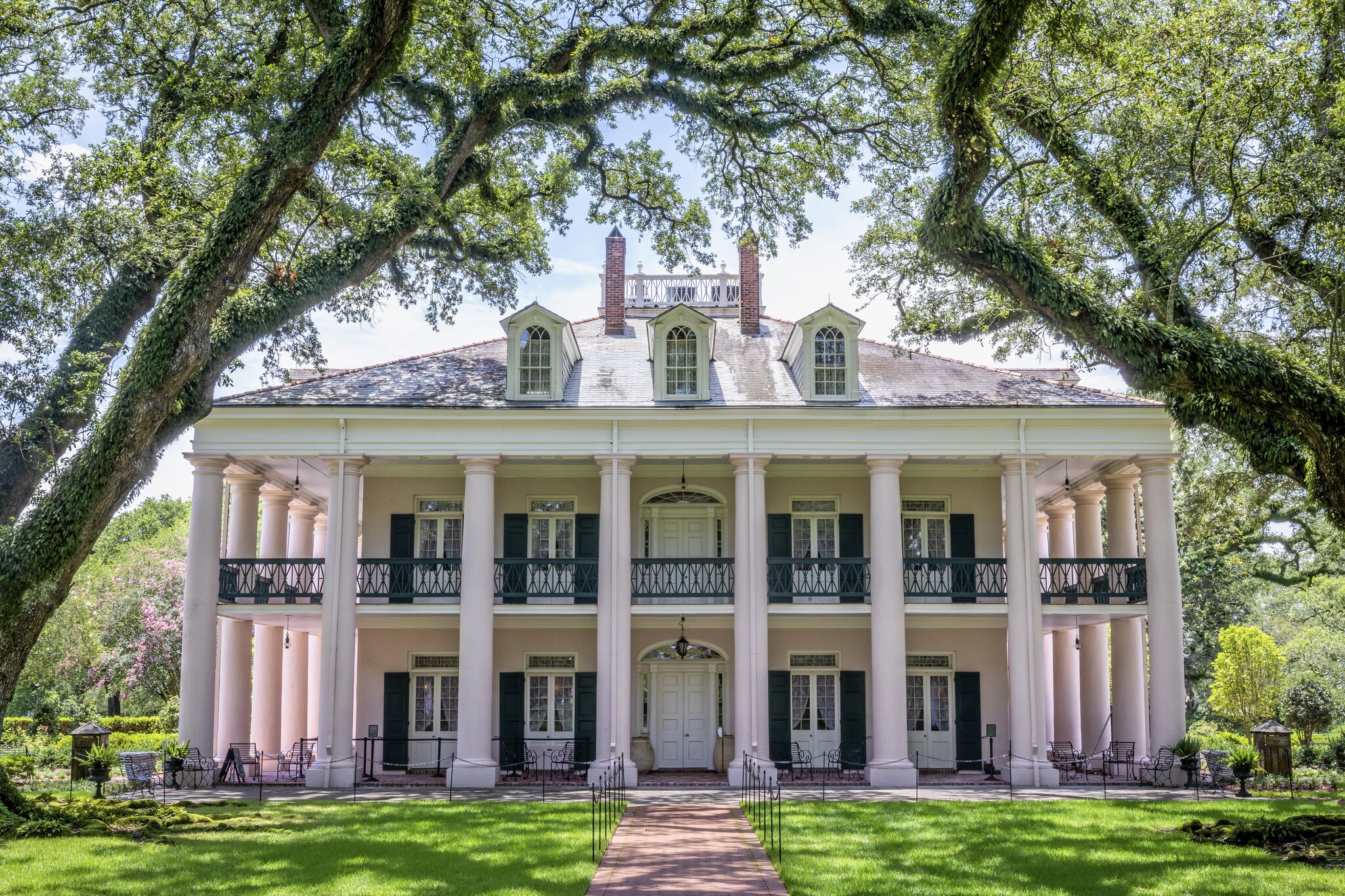 The exterior of Oak Alley Plantation’s great house, with slightly pink columns, framed by vine-laden trees.
