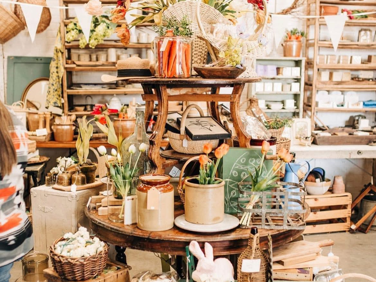 A cozy indoor display at Vintage Market Days featuring rustic wooden shelves, pottery, baskets, fresh tulips and curated vintage home décor items.