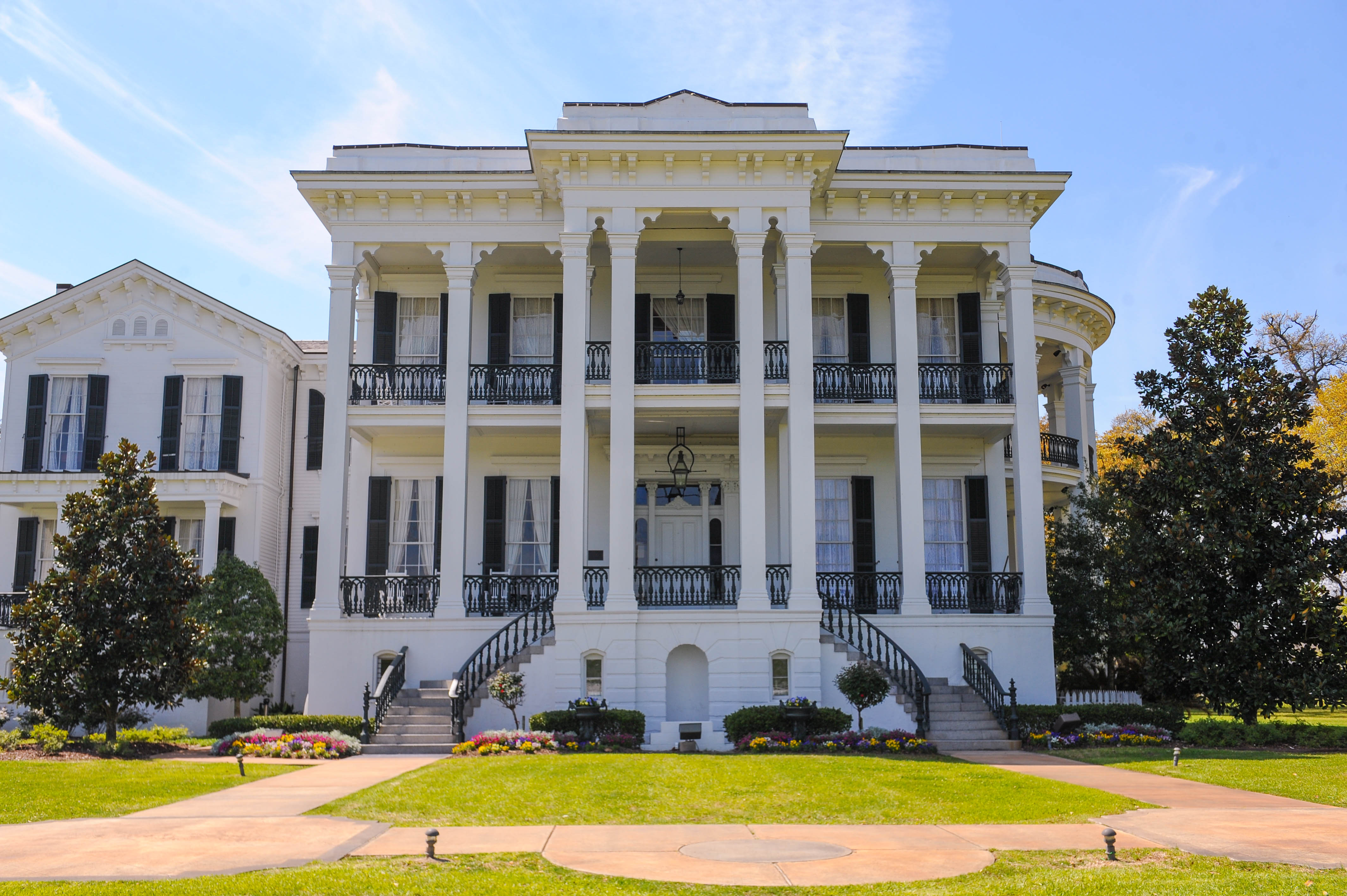 Exterior of a large, two-story white plantation house with columns and black iron balconies