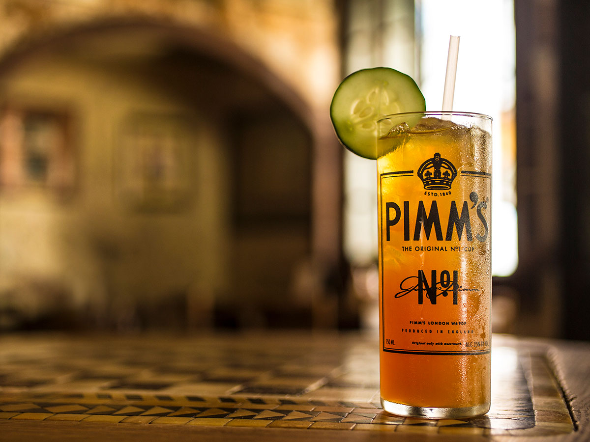 Pimms Cup cocktail from Napoleon House in New Orleans A vibrant orange cocktail, garnished with a cucumber slice, on a table at Napoleon House in New Orleans, Louisiana.