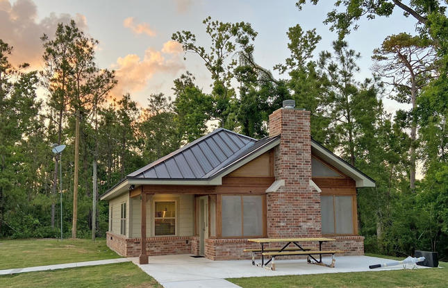 A mostly brick cabin at Sam Houston Jones State Park, with towering trees in the background and a light blue sky.