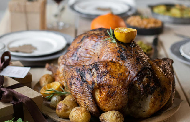 A perfectly roasted Louisiana turducken, topped with a sprig of thyme and half a lemon, surrounded by roasted potatoes, on a neatly set Thanksgiving table.