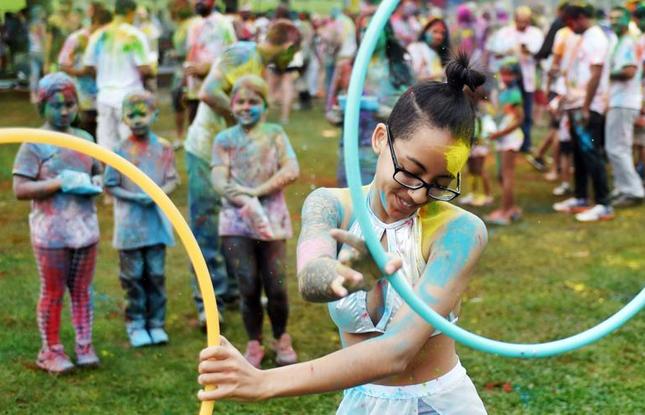 Children — covered in Holi Festival powder — watch as a performer hula hoops.
