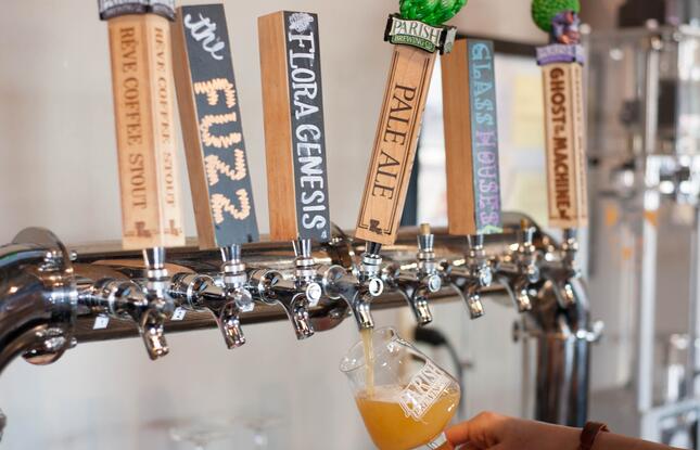 A person pours a hazy draft beer from a row of custom tap handles at Parish Brewing Company.