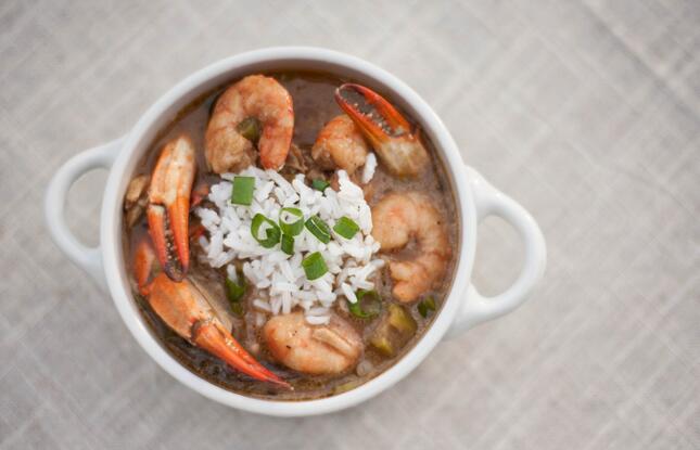 A pot of seafood gumbo with shrimp, crab, rice and green onions.