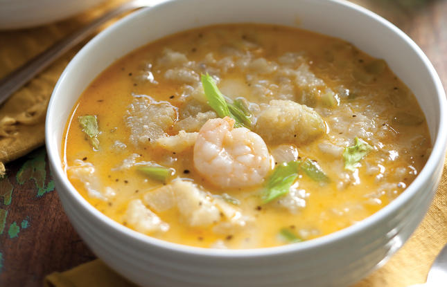 A white bowl of mirliton and shrimp soup, with perfectly pink shrimp peeking through the orange broth.