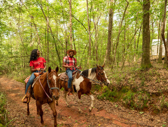 Two people ride horses through a dirt trail at Bogue Chitto State Park.