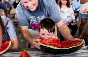 A child eats a watermelon as a mentor stands by.
