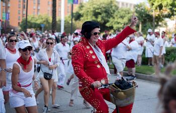 A person, dressed as Elvis in a red suit, rides a bike through New Orleans.