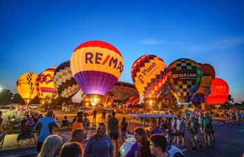 Dozens of vibrant balloons rise in the night sky at Red River Balloon Rally.