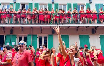 Dozens of people, all wearing red dresses, socialize in the streets of New Orleans. 