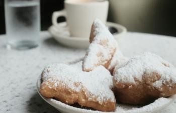 a vegan beignet on a plate with a coffee cup behind it 