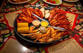 A large platter of seafood, including crawfish, corn and potatoes on a brightly decorated table at Boudreau & Thibodeau’s Cajun Cookin’.