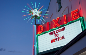 The brightly lit Dixie Theater marquee glows at dusk with a sign reading “Welcome to Ruston.”