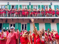 Dozens of people, all wearing red dresses, socialize in the streets of New Orleans.
