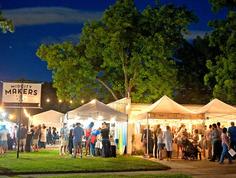 A crowd shops at different vendors, each hosted within a white tent. Lights are strung throughout the scene.