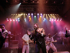The Commodores perform on stage. Multicolored stage lights illuminate the lead singer.
