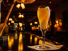 A sparkling French 75 cocktail in a champagne flute, glowing under warm bar lights at Arnaud’s Restaurant.