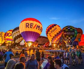 Dozens of vibrant balloons rise in the night sky at Red River Balloon Rally.