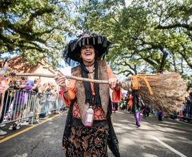 A person dressed as a witch holds a broomstick, parading down a street at Rougarou Festival.