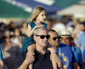 A parent with their child on their shoulders watches a performance at Jazz Fest.