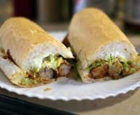 A po'boy on a white-bread roll is cut in half on a white paper plate at Domilise's Po-boys &amp; Bar in New Orleans, Louisiana.
